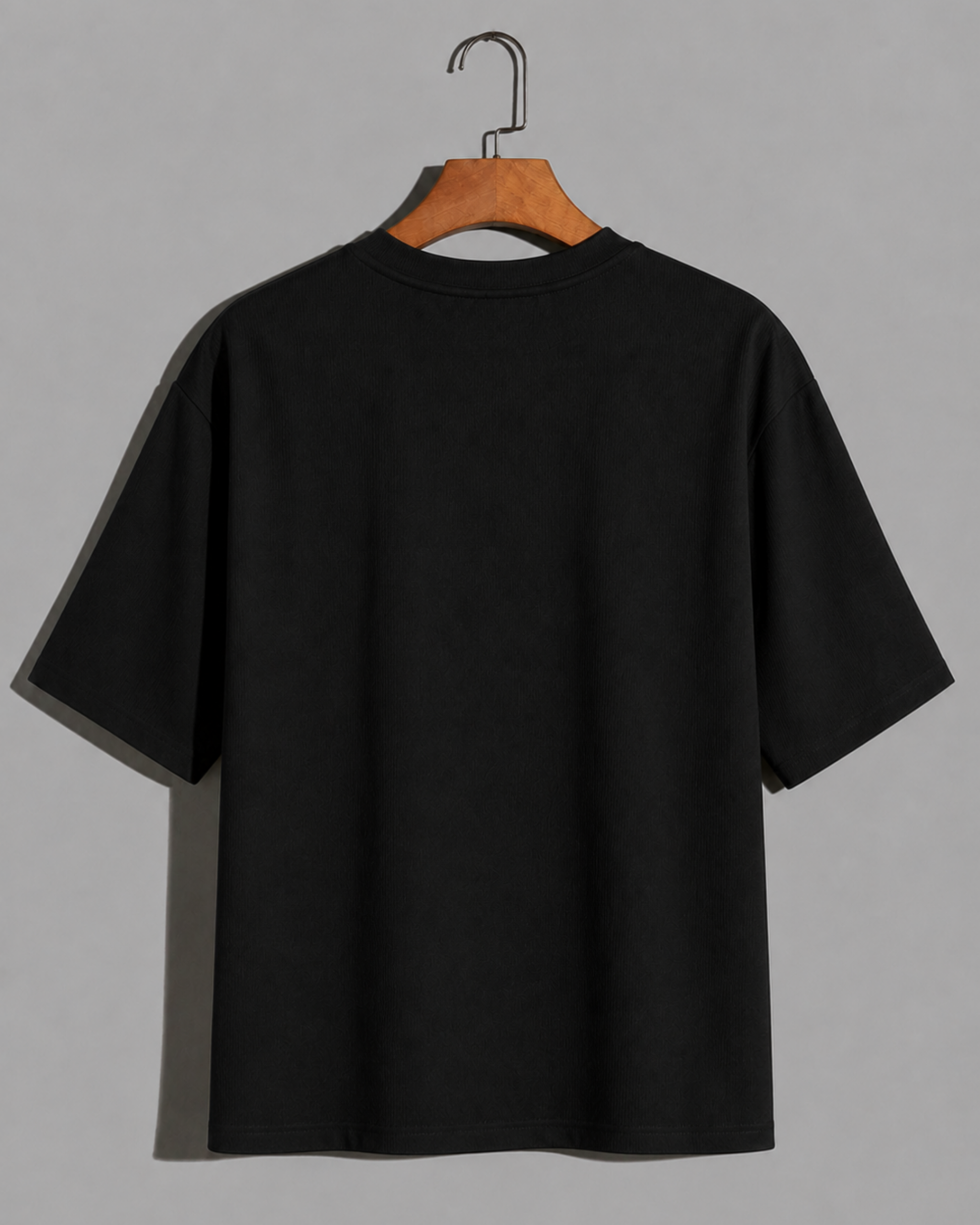 Back view of a Black oversized t-shirt with white VenomX logo on chest, hanging on wooden hanger, premium minimalist streetwear design